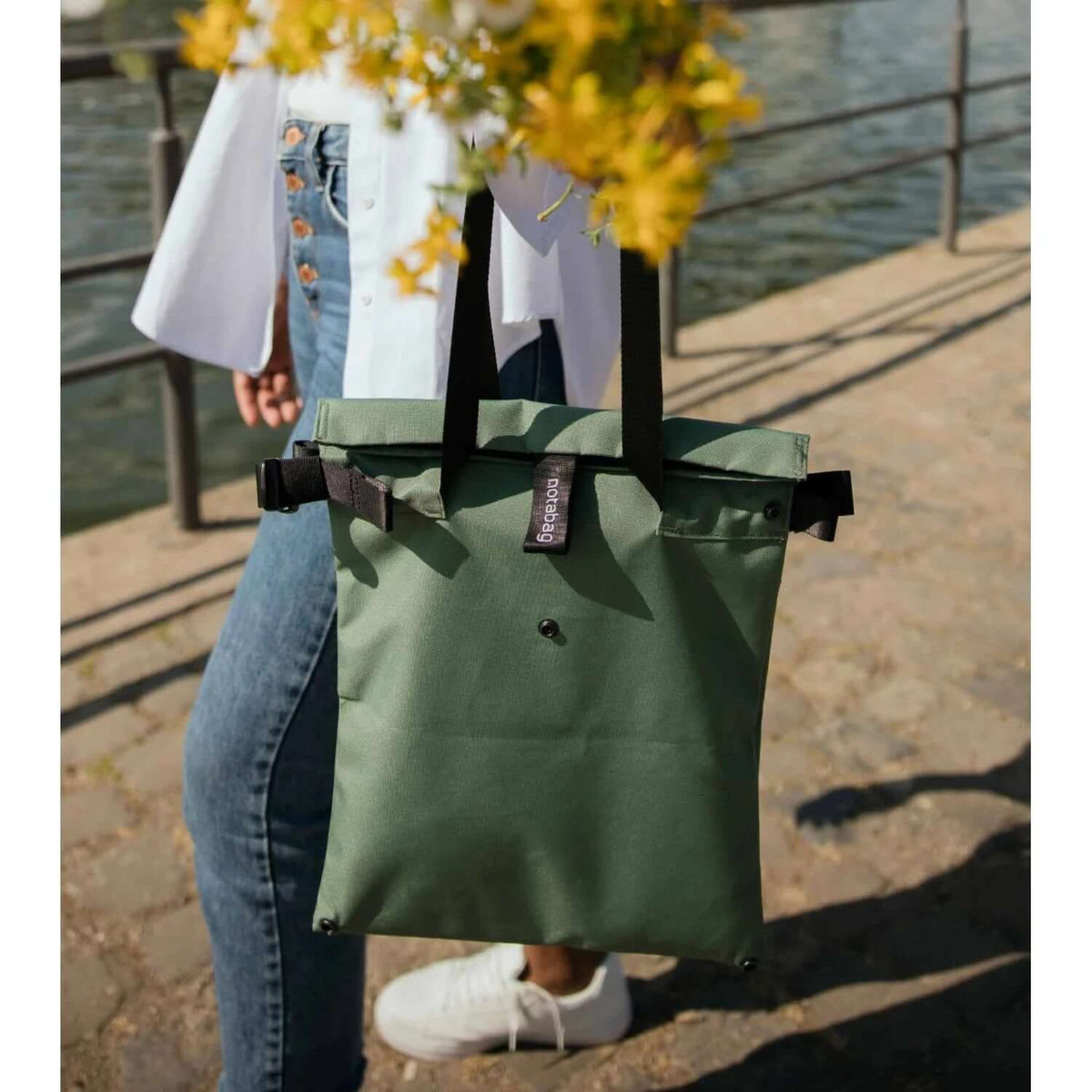Notabag Crossbody Tote in green being carried by a person near a body of water, showcasing its versatile design.