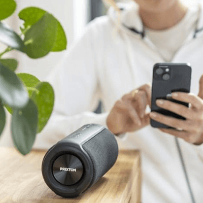 Prixton Echo Box Speaker placed on a table with a person using a smartphone in the background.