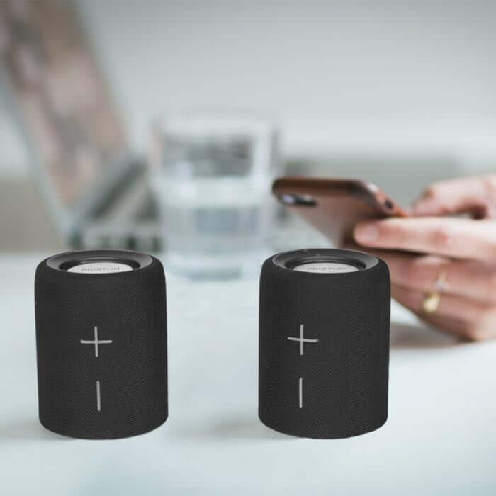 Prixton Aloha Lite Bluetooth Speaker in a stylish black design on a table with a smartphone.