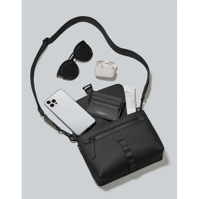 Gaston Luga Splash Crossbody Bag with sunglasses, phone, and AirPods on gray background.