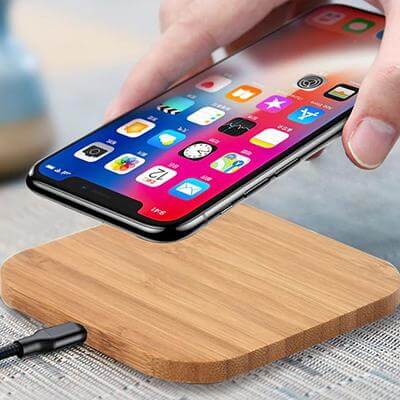 Phone being placed on a rectangular wood-finish charging pad connected by a cable