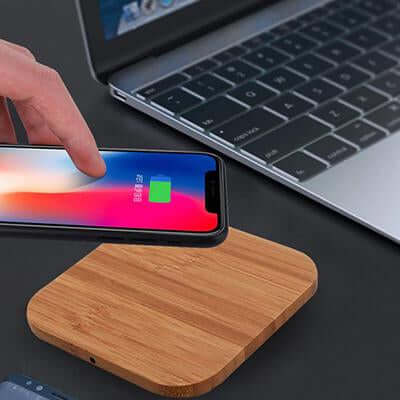 Phone placed on a wood-finish charging pad beside a laptop, with a cable connected