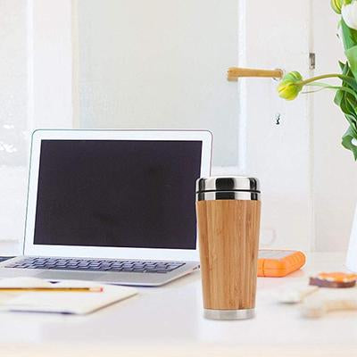 Covered bamboo coffee mug on a desk beside a laptop