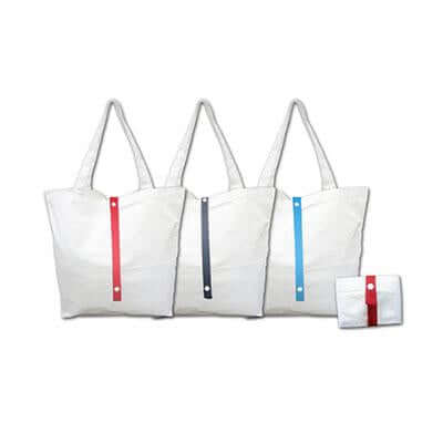 Natural-coloured canvas tote bags with red, dark and blue fastening straps, beside a folded red-strap bag